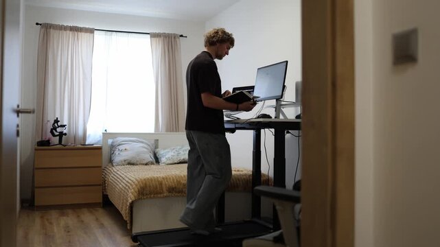Young professional reads a book while walking at his computer workstation combining self education with movement to stay active focused and productive during work hour on