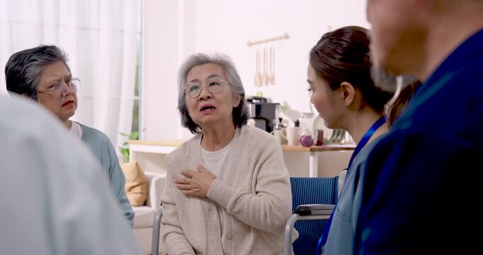 Asian senior woman discusses health and rehabilitation needs with Asian female nurse and senior peers in assisted living center, receiving support, wellness guidance and compassionate daily care.
