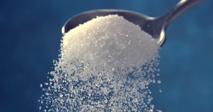 Sugar falling from a spoon in slow motion on blue background
