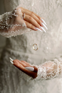 Gold wedding ring suspended between a bride's elegant hands in a white lace dress, creative bridal jewelry and marriage concept.