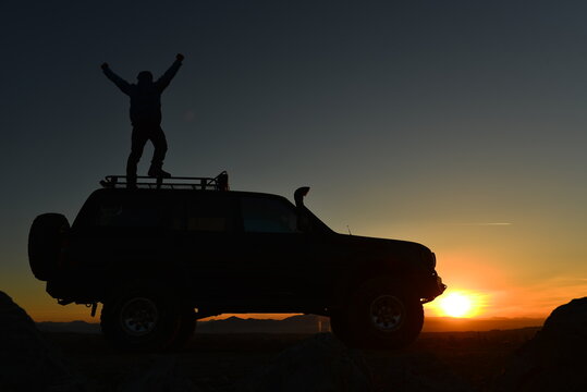 Traveler Standing on a 4x4 SUV Against the Sunset