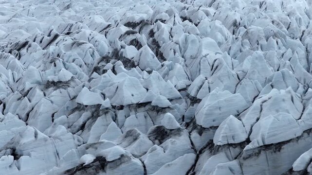 Solheimajokull glacier showing densely fractured ice blocks, deep crevasses, flow deformation and dark volcanic sediment bands in South Iceland, drone slide descent