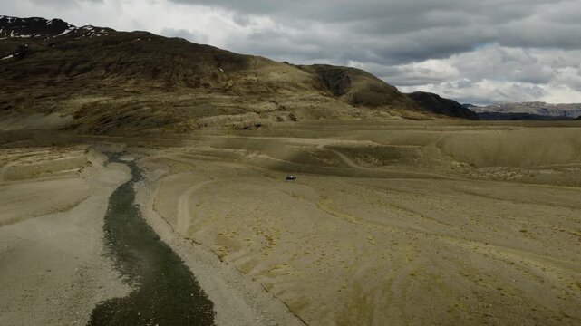 SUV crossing a discontinuous gravel track through the barren Odadahraun volcanic desert below the Dyngjufjoll ridge on the Askja route, North Iceland, drone forward flyover descent