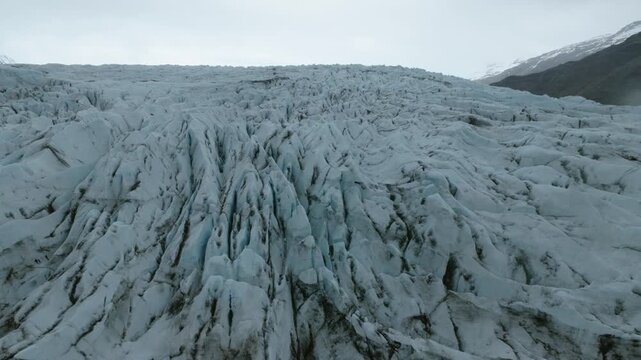 S&oacute;lheimaj&ouml;kull outlet glacier with dense longitudinal and transverse crevasses, flow fractures and compacted glacial ice beneath a volcanic mountain ridge in South Iceland, drone descent