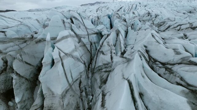 Heavily crevassed glacier ice with deep fractures, folded flow structures, dark sediment and compact blue-white ice, southeastern Iceland, Vatnajokull region, drone forward flyover