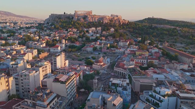 Magnificent aerial view of the ancient Acropolis of Athens and the Parthenon citadel, gracefully perched on a rocky outcrop above the modern city during a beautiful and warm sunset