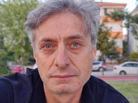 Contemplative portrait of a serious middle-aged man in a park, reflecting on life's passage, his blue eyes showing both wisdom and the weight of experience.