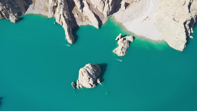 Aerial high-angle view over turquoise emerald waters of alpine Lake Kel-Suu surrounded by sheer limestone cliffs, Kyrgyzstan