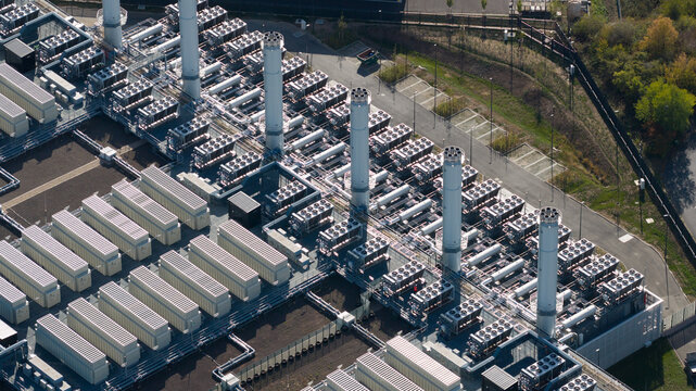 Aerial view of a large industrial power facility with cooling towers, rows of electrical equipment, and storage units in Dietzenbach, Hessen, Germany.