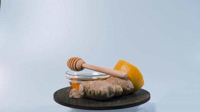 Honey in a glass bowl turns beside ginger slices and half a lemon on a wooden stand. Seasonal wellness and natural comfort food traditions concept