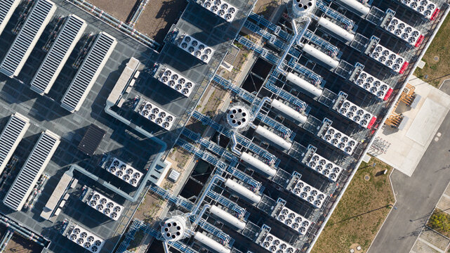 Aerial view of an industrial facility featuring rows of cooling fans, complex piping systems, and technical infrastructure in Dietzenbach, Hessen, Germany.