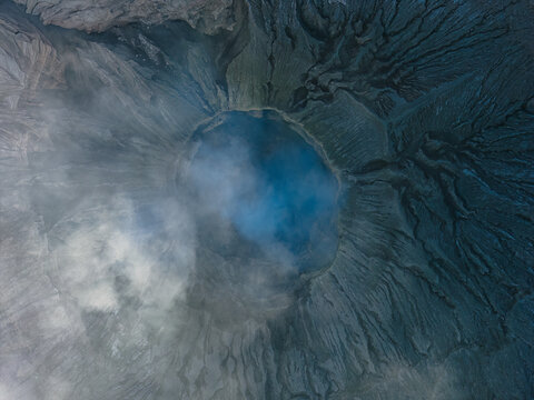 Aerial view of the crater of Mount Bromo with volcanic ash, rugged textures, and swirling smoke in Kecamatan Kademangan, Jawa Timur, Indonesia.