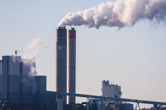 An industrial plant with tall, smoking chimneys set against a clear sky, symbolizing manufacturing, energy production, or environmental pollution