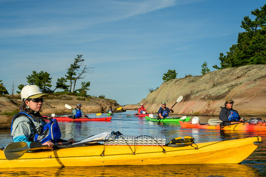Sea kayaker in a yellow tandem kayak with a group of paddlers behind in a granite channel with copy space on Georgian Bay, Ontario, Canada
