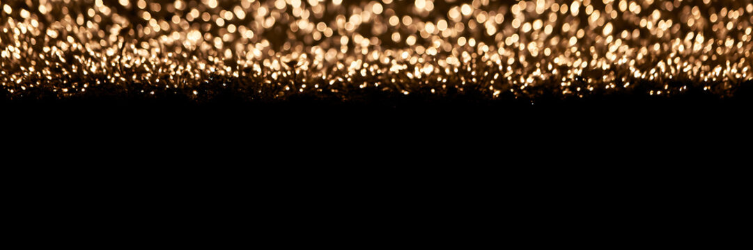 Abstract golden bokeh lights on a solid black background. Panoramic banner with glowing blurred texture and dark negative space. Festive holiday backdrop. Luxury overlay effects