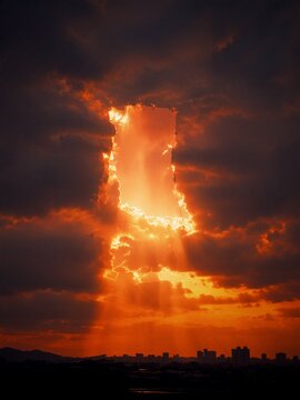 Rectangular opening in dramatic storm clouds above a city skyline, glowing sunset and breakthrough light concept