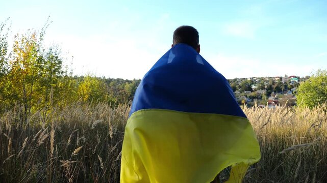 Military man in uniform stands with raised over head flag of Ukraine at countryside. Male ukrainian army soldier with lifted national banner in honor of victory against russian aggression. End of war