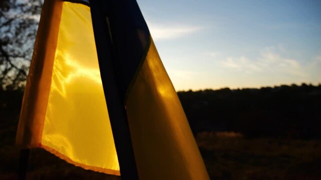 Blue-yellow symbol of Ukraine waving at wind against the background of sunlight. Ukrainian flag illuminated by sun fluttering at countryside. Concept of peace and support against russian aggression
