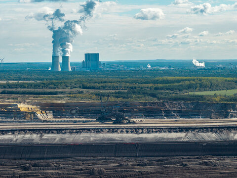 Aerial view of Tagebau Welzow-Sud brown coal open-pit mine with deep excavation layers, heavy machinery, and a power plant emitting smoke in the distance, Spremberg, Brandenburg, Germany.
