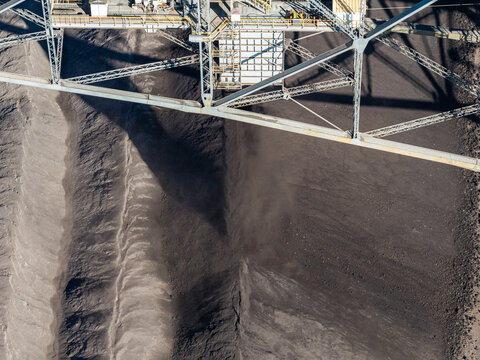 Aerial view of the Tagebau Welzow-Sud brown coal open-pit mine with its massive industrial excavator structure casting shadows over the dark excavated earth in Spremberg, Brandenburg, Germany.
