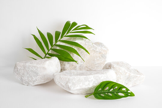 White stones and green palm leaves on white background for spa and wellness decor