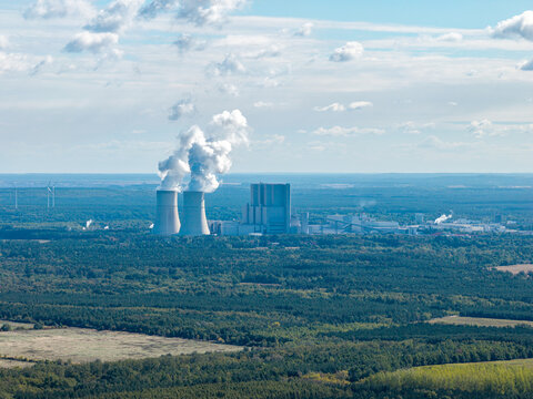 Aerial view of the Schwarze Pumpe power station with its cooling towers emitting steam, surrounded by vast forests and open landscape in Spremberg, Brandenburg, Germany.