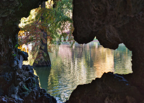 Warm late-afternoon light reflects on the pond beside the Crystal Palace in Retiro Park, Madrid, Spain. Trees and dark foreground shadows frame the tranquil water.