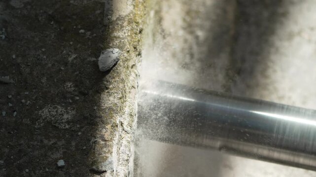 Heavy-duty rotary drill bit boring through solid concrete block inside building under renovation. Macro shot.