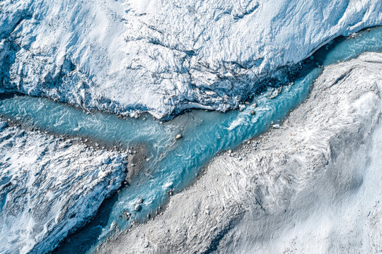 Aerial perspective of the Rhone Glacier covered with white protective sheets, showcasing the icy blue river cutting through the snowy landscape, highlighting glacier preservation efforts.