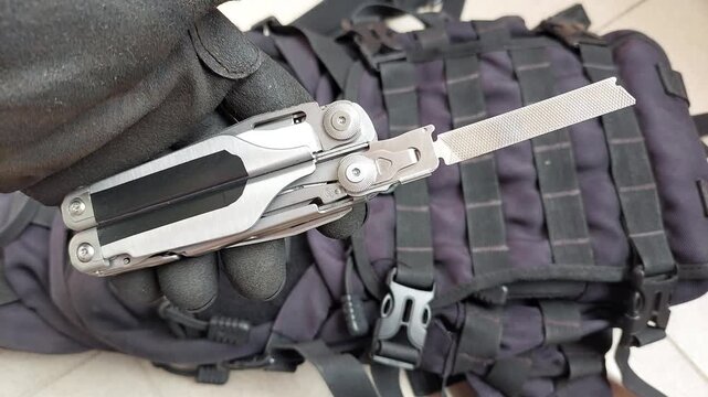 Close up top view shot of a gloved hand opening a metal file blade on a heavy duty stainless steel multitool against black tactical background. Concept of metalworking, finishing tools, repair, craft