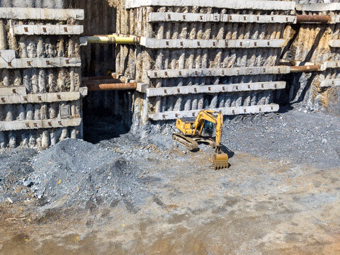 Aerial view of a deep construction excavation site with concrete retaining walls, steel struts, and a yellow excavator on gravel ground in Istanbul, Istanbul, Turkiye.