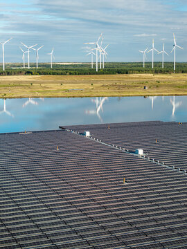 Aerial view of the floating solar park at Cottbuser Ostsee with rows of photovoltaic panels on the water, wind turbines in the background, and green landscape in Cottbus, Brandenburg, Germany.