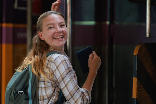 Happy young woman traveling by train, holding a passport and smiling, enjoying a vacation journey, a backpacker arriving at her destination for an adventure
