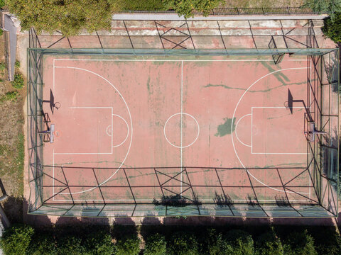 Aerial view of a red basketball court with white markings, enclosed by a green chain-link fence, surrounded by trees in Istanbul, Istanbul, Turkiye.