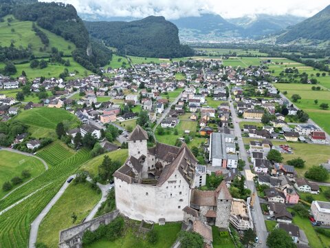 Aerial view of Gutenberg Castle surrounded by the village of Balzers, lush green hills, and mountains in Liechtenstein.