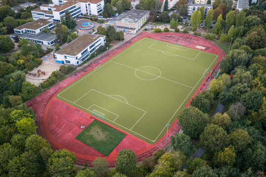 Aerial view of the High-Deck-Siedlung soccer field with a red running track surrounded by lush trees and residential buildings in Berlin, Berlin, Germany.