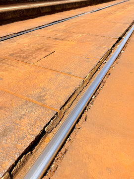Close view of tram rails running through weathered orange pavement in Takaramachi, Nagasaki, Japan. The parallel tracks and raised paving edges create strong diagonal lines in sunlight.

