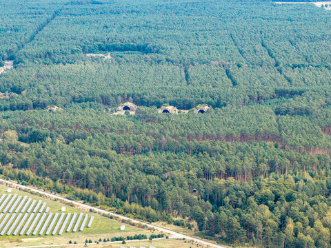 Aerial view of the solar farm at the former Preschen military airfield, featuring historic hardened aircraft shelters nestled within a pine forest in Neisse-Malxetal, Brandenburg, Germany.