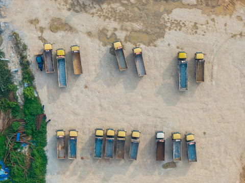 Aerial view of a construction area with rows of yellow dump trucks parked on a dirt ground in Bukit Tambun, Penang, Malaysia.