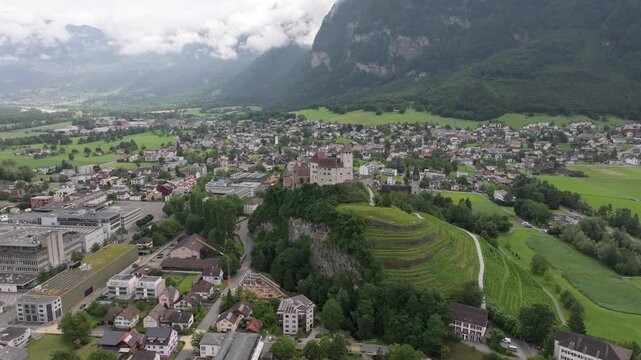 Aerial view of Vaduz Castle overlooking the town of Vaduz with lush green hills and mountains in the background in Liechtenstein.