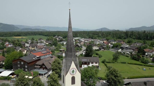 Aerial view of a church spire rising above a village with green fields and houses in Liechtenstein.