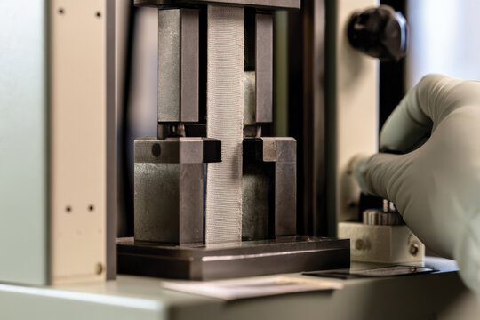 An industrial testing machine is set up to measure the strength and durability of materials, with close attention given to the testing process by a gloved hand.