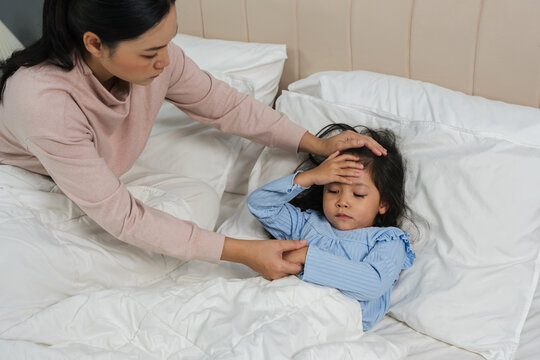 mother comforting sick daughter while touching her forehead with fever headache in bed