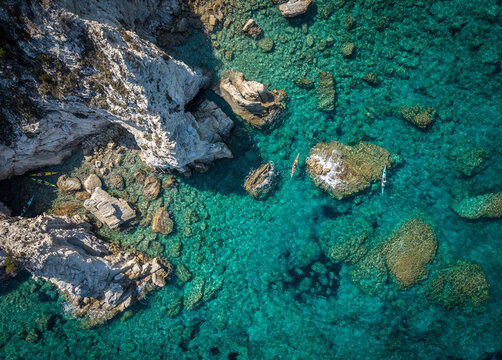 Aerial view of kayakers paddling through clear turquoise waters along the rocky coastline near Lakka, Paxos, Ionian Islands, Greece