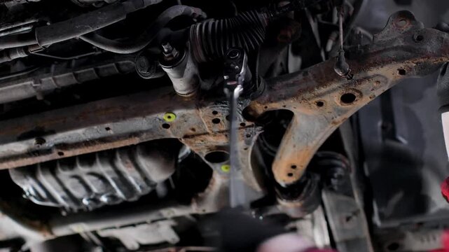 Close up of mechanic loosening a suspension bolt under a car with a breaker bar ratchet wrench static shot.