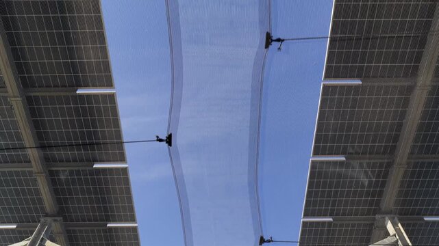 Aerial view of solar panels installed on a structure with a clear blue sky visible between them in Faenza, Emilia-Romagna, Italy.