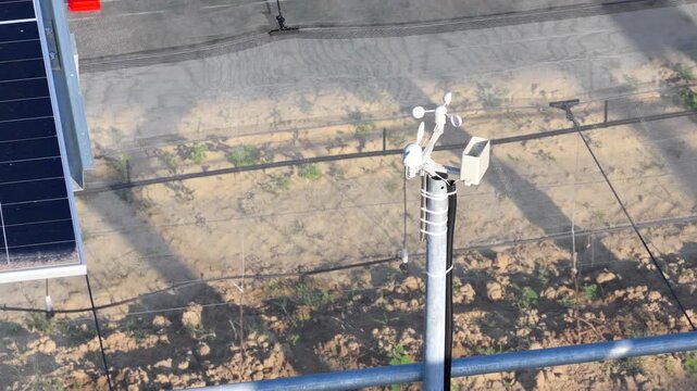 Aerial view of an anemometer mounted on a pole in a field covered by protective agricultural netting in Faenza, Emilia-Romagna, Italy.