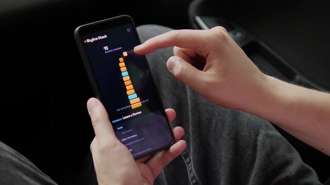 Person plays a mobile block-stacking game until the tower collapses, capturing casual gaming, touchscreen entertainment, digital focus and the growing appeal of skill-based apps.
