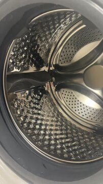 Vertical close up shot of clean empty shiny stainless steel drum inside washing machine appliance before loading dirty clothes or laundry for cycle. High quality 4k footage