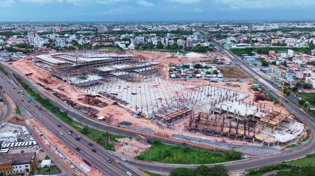 Construction workers and heavy equipment building City Center shopping mall along Las Americas highway in Santo Domingo Este, Dominican Republic, aerial slow push-in shot